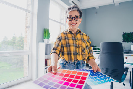 Photo of nice retired woman hold samples palette designer wear plaid shirt comfortable modern office loft room interior indoors workspaceの写真素材