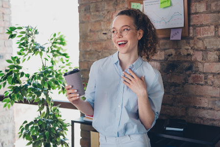 Young professional woman smiling with coffee in modern office setting near a brick wall and charts