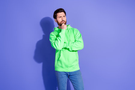 Photo of handsome mature age funky man wearing bright green hoodie sportswear touch chin pensive standing isolated on violet color backgroundの写真素材
