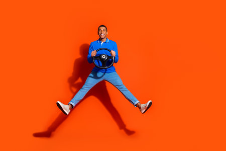 Happy young man holding steering wheel on vibrant orange background