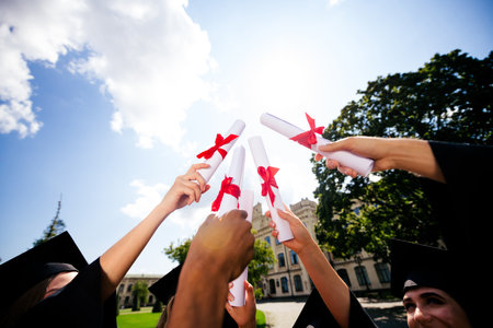 First person view portrait of group students raise diploma document sky mortarboard gown graduation university building outdoorsの写真素材