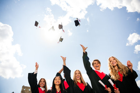 Joyful group of graduates celebrating their achievement by tossing caps in the air on a sunny dayの写真素材