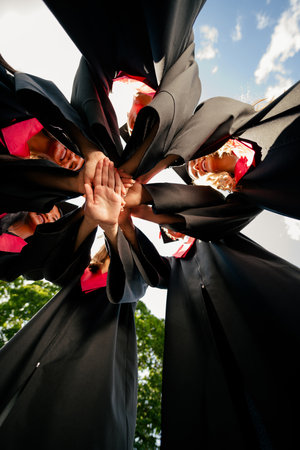 Low angle view vertical portrait of group students pile stack handshake mortarboard gown graduation...