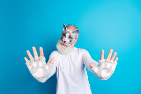 Elderly gentleman posing with cat-themed costume and a cheerful expression against a vibrant blue backgroundの写真素材