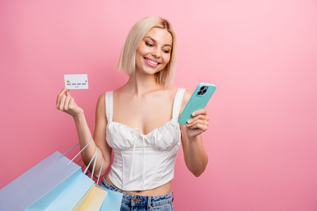 Stylish young woman holding a credit card and shopping bags while using her smartphone against a...