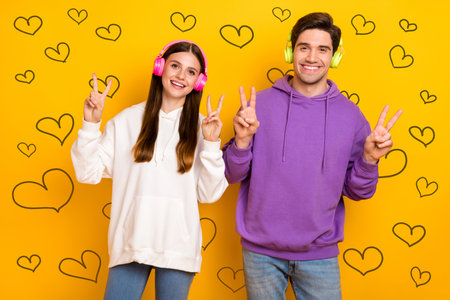 Portrait of funny attractive lady handsome guy show v-sign enjoy mp3 sound isolated on yellow color...