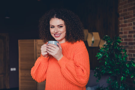 Photo of pretty young woman hold coffee cup wear orange pullover loft interior apartment indoorsの写真素材