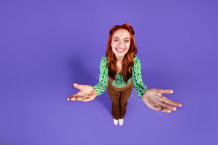 Red-haired young woman reaching out on vibrant purple background conveying happiness and styleの写真素材