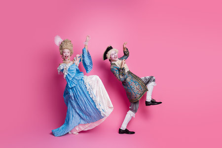 Elegant couple in baroque costumes having fun against vibrant pink background, showcasing classic fashionの写真素材