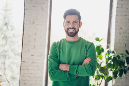 Relaxed man in green sweater smiling at home, daytime interiorの写真素材