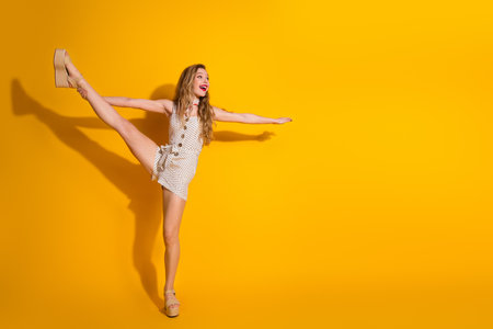 Cheerful young woman in polka dot dress posing elegantly against vibrant yellow backgroundの写真素材