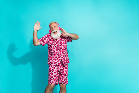 Photo of handsome bearded grandpa sing listen music dressed stylish pink leopard print garment isolated on cyan color backgroundの写真素材