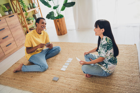 Photo of lovely cheerful couple wife and husband sit floor play poker game cards relax rest indoors...