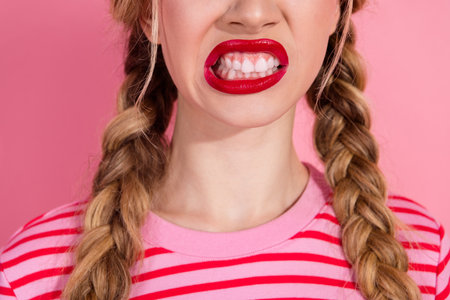 Charming young woman with a playful expression showing off her vibrant red lips against a pink backdrop.の写真素材