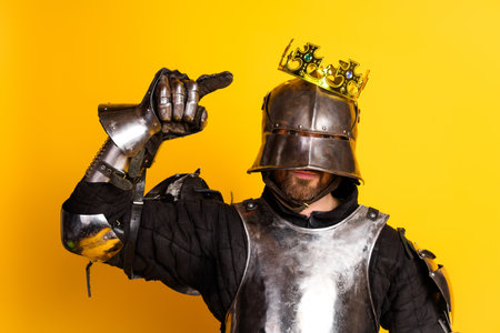 Medieval knight in royal crown posing against bright yellow background portraying bravery and refinementの写真素材
