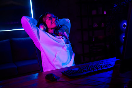 Young woman enjoying a relaxed gaming session indoors with neon lights highlighting vibrant colorsの写真素材