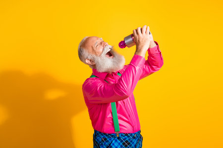 Photo of nice senior male sing karaoke wear pink shirt plaid pants suspenders fancy outfit isolated on yellow color backgroundの写真素材