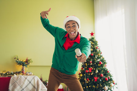 Photo of handsome good mood guy wear green sweater enjoying singing carols celebrating noel xmas indoors room home houseの写真素材