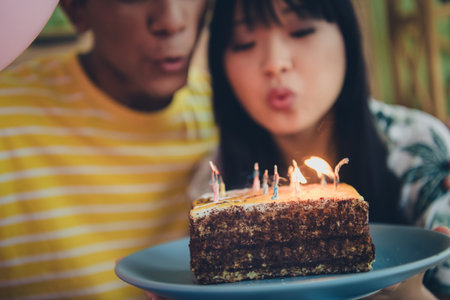 Photo of multiethnic pretty sweet couple family celebrate anniversary birthday hold cake blow out candles indoors apartmentの写真素材