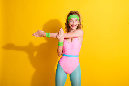 Young woman in retro sportswear stretching her arms with a bright smile against a yellow backdrop