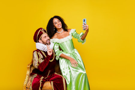 Couple in vintage costumes taking a selfie with yellow background, blending historic and modern vibesの写真素材