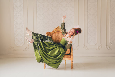 Elegant young woman in a vintage green dress in a royal interior exudes aristocratic charm with a touch of humorの写真素材