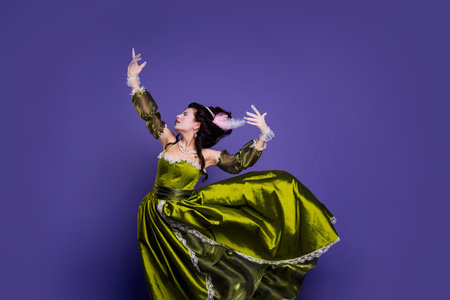 Elegantly styled woman in green baroque dress posing against purple background showcasing a historical and regal themeの写真素材