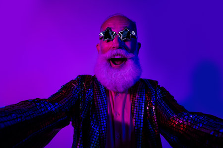 Photo of cool macho senior male take selfie photo dressed colorful sequins striped garment isolated on blue purple neon light backgroundの写真素材
