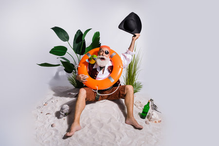Elderly pirate character on a sandy beach holding hat and enjoying an exotic holiday with tropical backdrop and beach accessoriesの写真素材