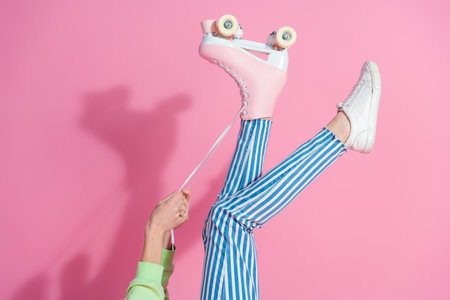 Stylish young woman tying laces of pink roller skate against a vibrant pink background, showcasing trendy fashion and leisure lifestyleの写真素材