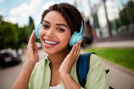 Cheerful woman in green shirt enjoying music outdoors with blue headphonesの写真素材