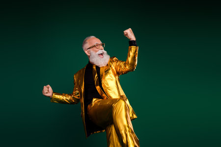 Charismatic elderly man in golden suit celebrating against a green backdropの写真素材
