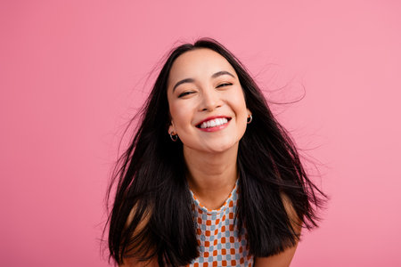 Charming young woman with brunette hair smiling joyfully against a vibrant pink background, showcasing trendy summer style and beauty.の写真素材
