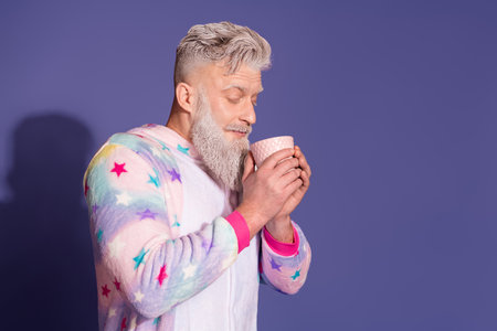 Trendy man in a unicorn pajama enjoying morning coffee against violet background