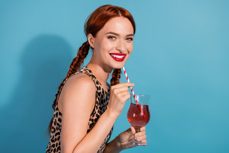Young woman with red braided hair enjoying a drink, smiling confidently against a vivid blue backgroundの写真素材