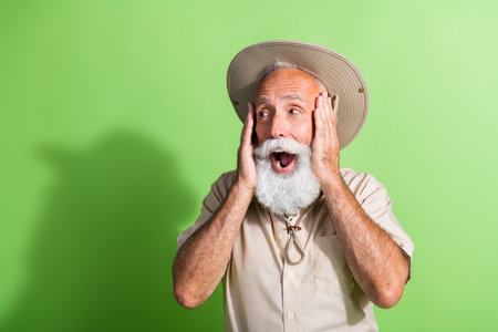 Photo of senior old man traveler touch face feel impressed look empty space isolated green color backgroundの写真素材