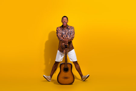 Young man with a guitar strikes a funny pose against a vibrant yellow backdropの写真素材