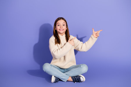 Happy girl dressed in casual sweater pointing sideways on a purple background, expressing excitementの写真素材