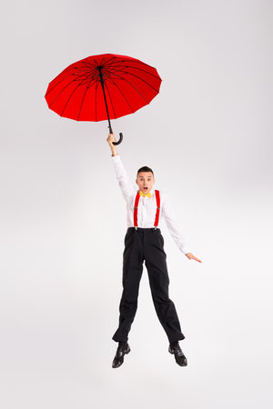 Young man dancing joyfully with red umbrella on white backgroundの写真素材