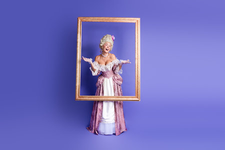 Elegant Woman in Historical Attire Posing Inside a Golden Frame Against Purple Backgroundの写真素材