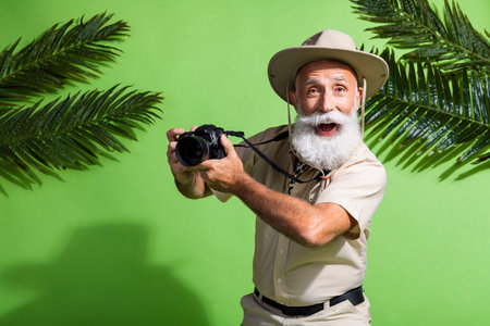 Photo of positive amazed adventurer senior man using digital camera showing isolated green color backgroundの写真素材