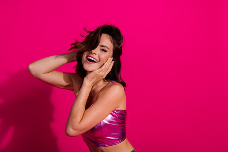 Brunette woman in shiny magenta top smiling against a bright pink backgroundの写真素材