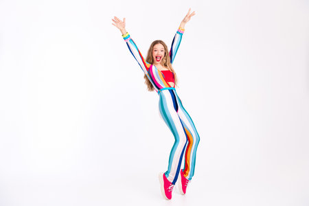 A vibrant young woman in a trendy striped outfit joyfully leaps against a white backdrop, embodying...