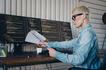 Female programmer analyzing code documents in a home office with modern equipmentの写真素材