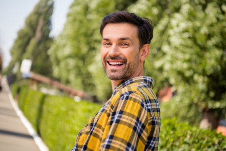 Smiling Young Man in a Checkered Yellow Shirt Outdoors in a Green Park on a Sunny Dayの写真素材