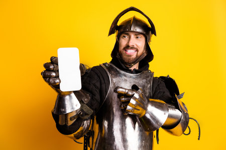 Smiling knight wearing armor holding smartphone with a yellow backgroundの写真素材