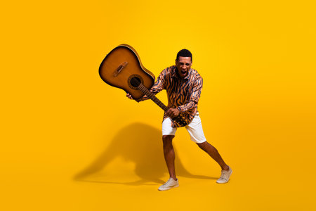 Young man enthusiastically playing guitar on vibrant yellow background symbolizing energy and passion for musicの写真素材