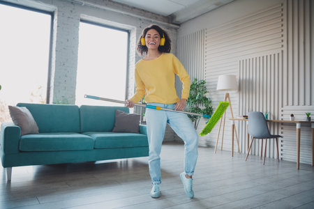 Young woman enjoying music and cleaning while having fun in a modern living room spaceの写真素材
