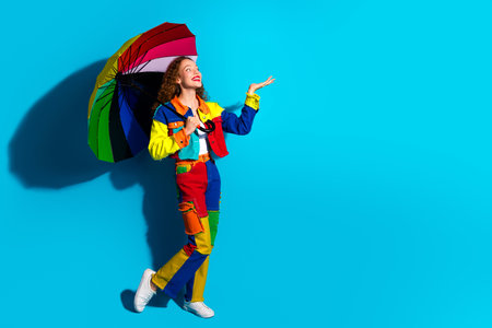 Colorful woman holding rainbow umbrella on vibrant blue background expressing happiness and funの写真素材
