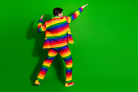 Young man in vibrant rainbow-striped suit posing confidently against a green background, embodying prideの写真素材